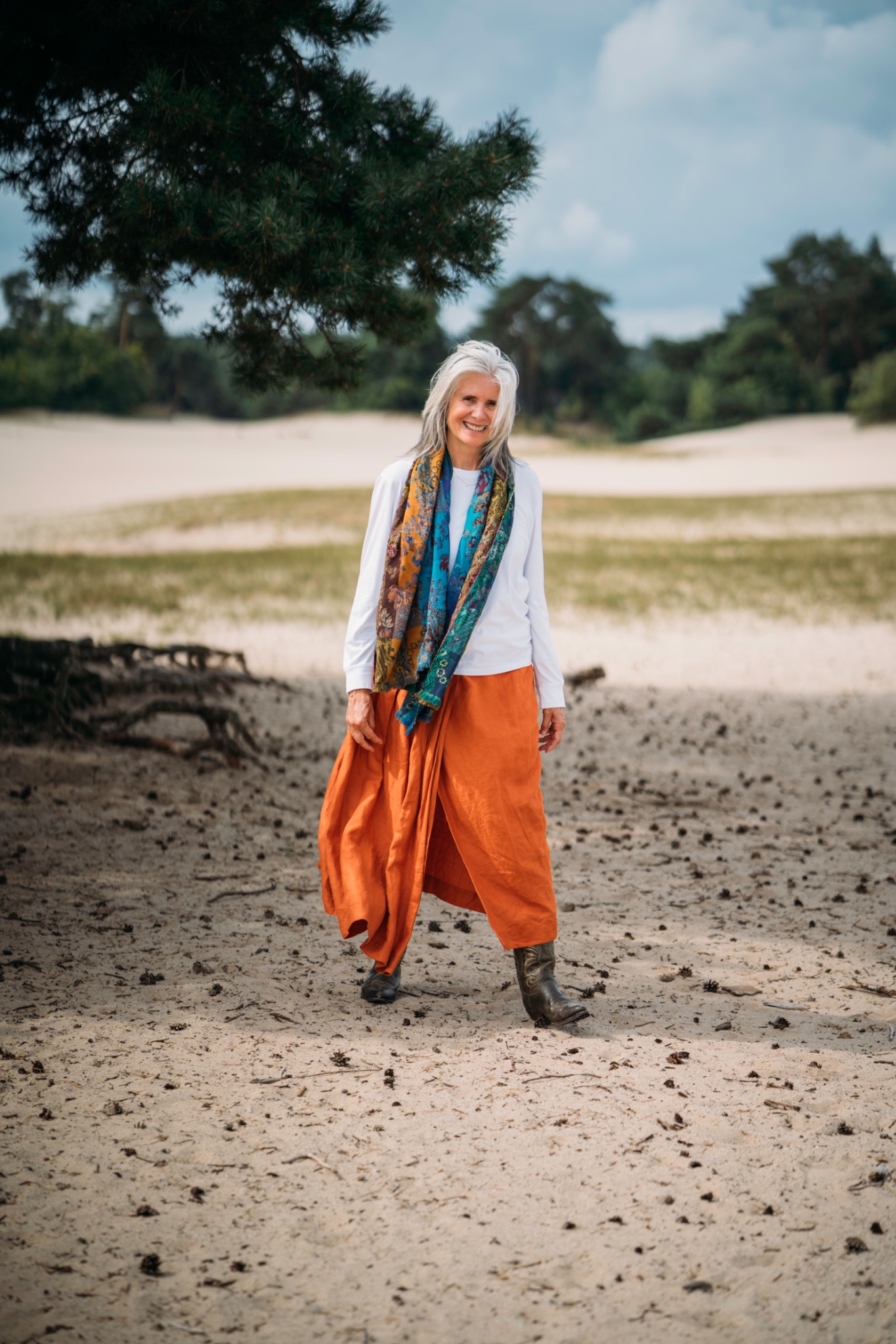 Ellen lachend in de duinen, met een oranje rok en een kleurrijke sjaal