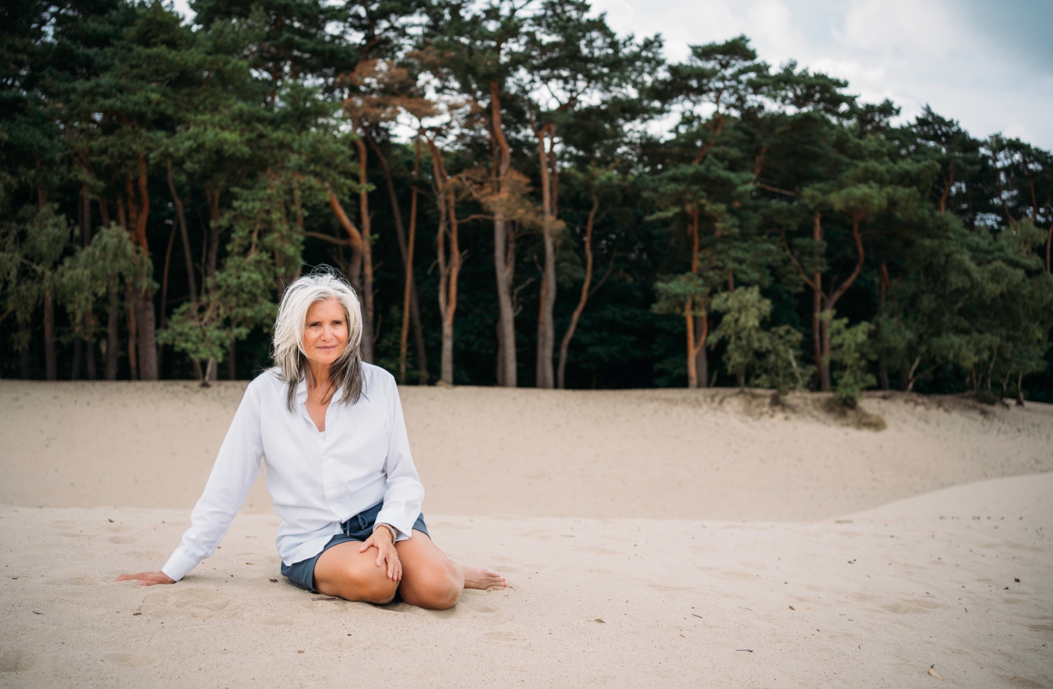 Ellen zit in het zand voor de bomen in de duinen